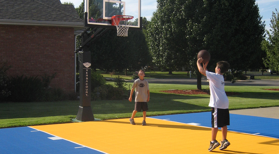 two boys playing basketball on their driveway basketball court of bright yellow and blue court tile