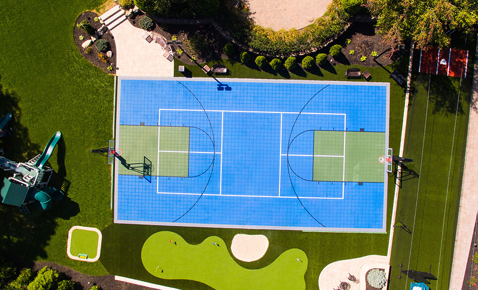 residential basketball court on gravel driveway surrounded by flowering bushes