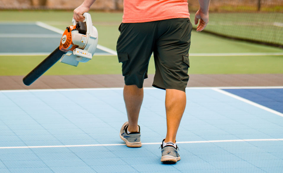 a man using a leaf blower to clean pickleball court